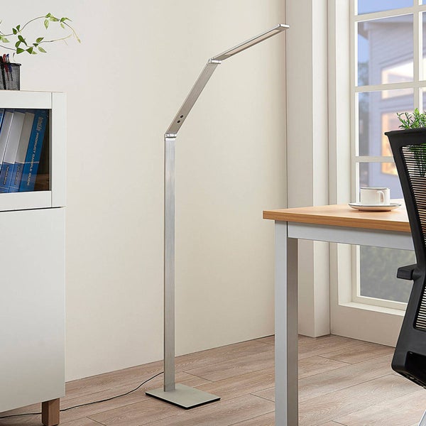 Moderne verstellbare LED-Stehleuchte aus gebürstetem Metall in einem hellen Büro neben Schreibtisch und Schrank.