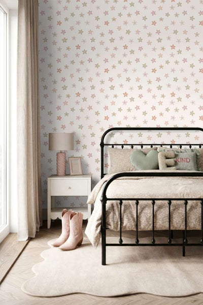 Ein Kinderzimmer mit einer Vliestapete mit Blumenmuster, einem schwarzen Metallbett und einem Nachttisch mit einer Tischlampe.