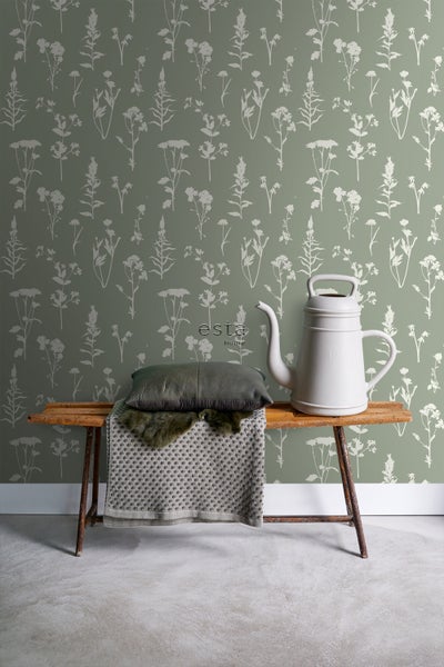 Dekoratives Stillleben mit Tapete mit Pflanzenmotiv, Kissen, Decke, Gießkanne und Bank