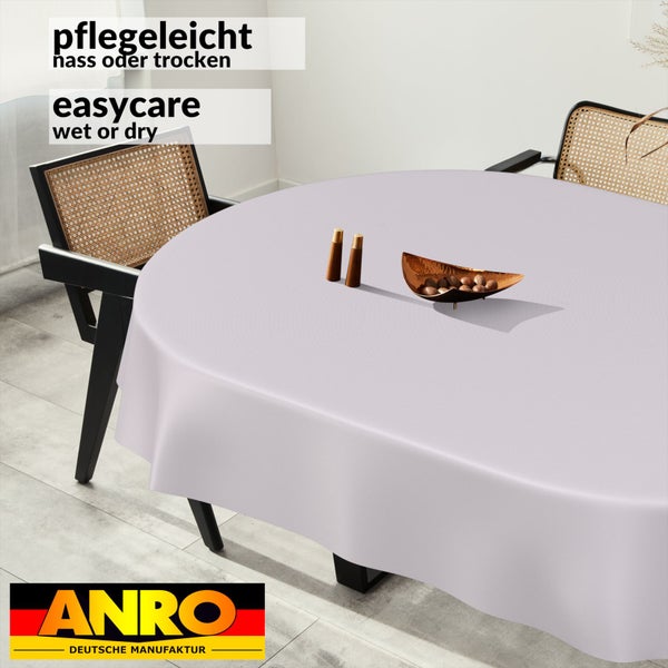 Rundes Tischtuch auf Esstisch mit Rattan-Stühlen in hellem Raum, pflegeleicht nass oder trocken, ANRO DEUTSCHE MANUFAKTUR Logo.