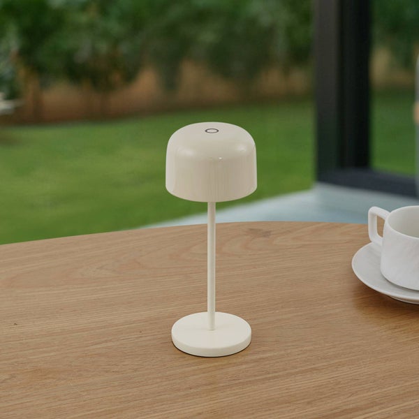 Moderne LED-Tischleuchte auf einem Holztisch im Außenbereich mit Gartenhintergrund.