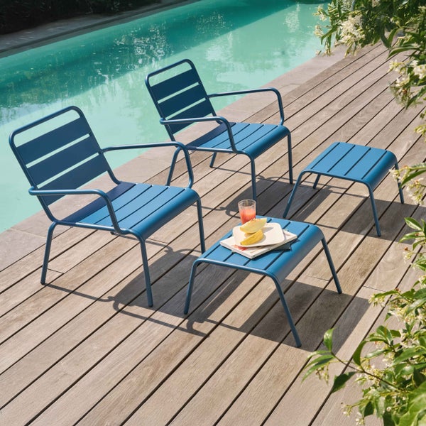 Helle, moderne Gartenlounge mit zwei Sesseln und Hockern aus Metall auf einem Holzdeck an einem Swimmingpool.