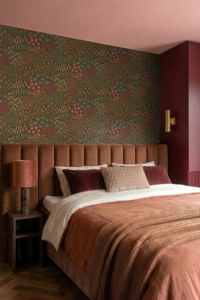 Gemusterte Tapete mit botanischen Motiven in einem Wohnzimmer mit Holzsideboard, Samtsessel und gemustertem Teppich.