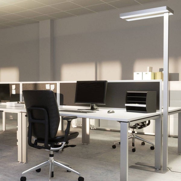 Moderne silberne LED-Bürostehleuchte in einem hellen Büro mit weißem Schreibtisch, schwarzem ergonomischem Stuhl und Computer.