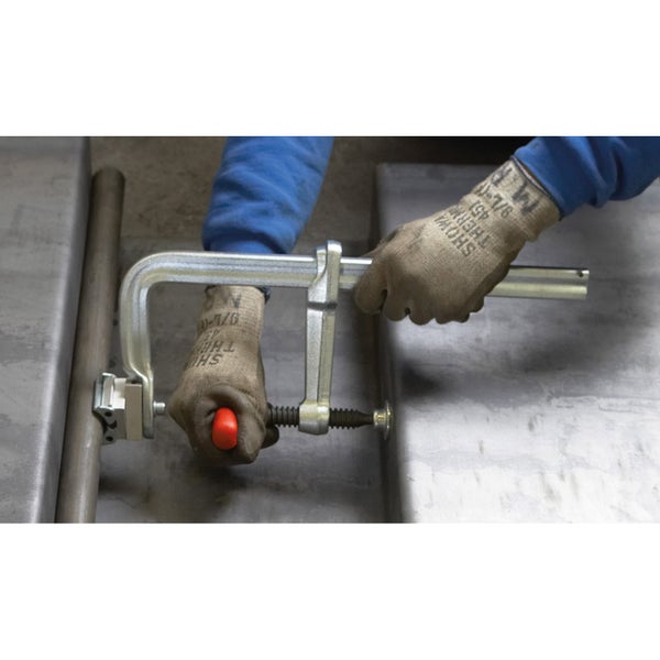 Eine Person schweißt Metallrohre mit Schweißgeräten und Schraubzwingen.