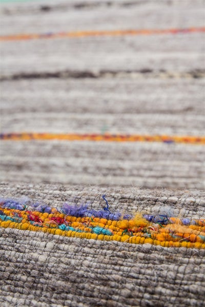 Detailansicht eines gewebten Teppichs mit horizontalen Streifen in Grau, Orange und Blau sowie grober Oberflächenstruktur.