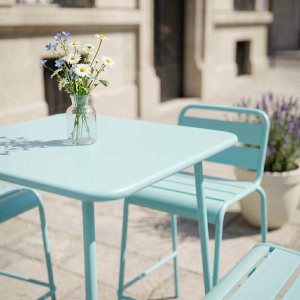 Hellblaues Bistro-Set aus Metall mit quadratischem Tisch und Stühlen im Außenbereich, auf dem Tisch steht eine kleine Glasvase mit Wildblumen.