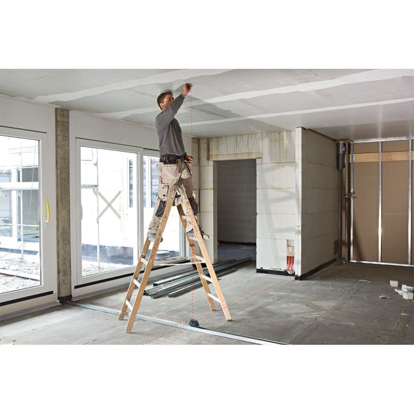 Mann auf Leiter misst Decke mit Laser-Entfernungsmesser in Rohbau