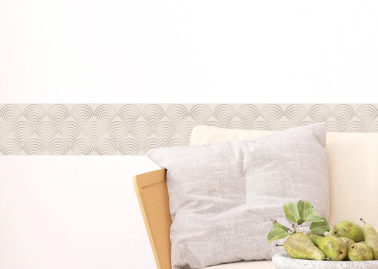 Helle Wand mit einer Tapetenbordüre mit Bogenmuster im Wohnzimmer mit Sessel, Beistelltisch und gestreiftem Teppich.