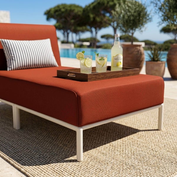 Moderne Gartenliege mit rostbraunem Polster, weißem Gestell und gestreiftem Dekokissen im Außenbereich am Pool auf einem Outdoorteppich.