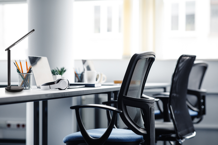 Moderne LED-Schreibtischleuchte auf einem Schreibtisch in einem hellen, organisierten Büro mit ergonomischen Stühlen.