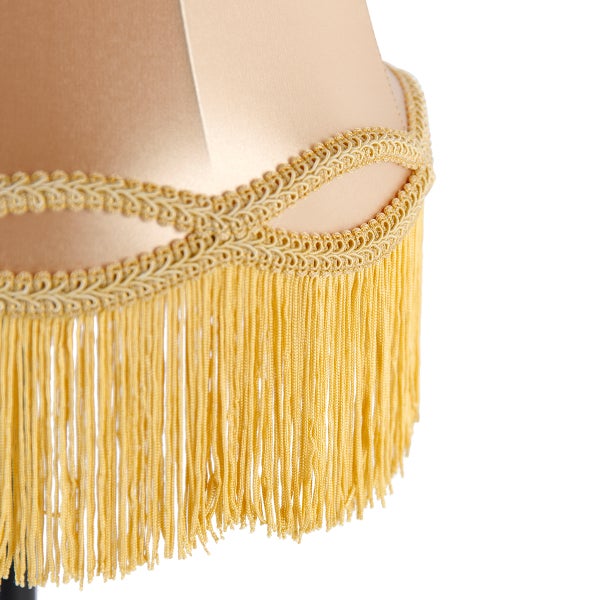 Detailansicht eines beigen Stofflampenschirms mit dekorativer Borte und langen Fransen.