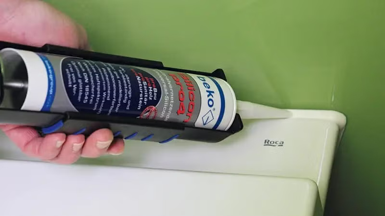 Hand hält Kartuschenpistole mit beko Silikon bei der Anwendung an einer sanitären Keramikfuge