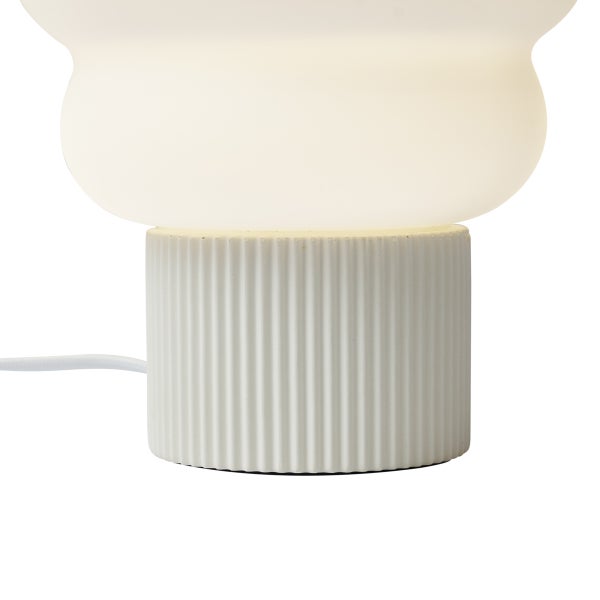 Tischleuchte mit geriffeltem zylindrischem Sockel und bauchigem weißem Schirm.