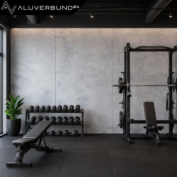 Modernes Fitnessstudio mit Aluverbund 24 Wandverkleidung in Betonoptik, Hantelbank, Hantelständer mit Kurzhanteln und Power Rack.