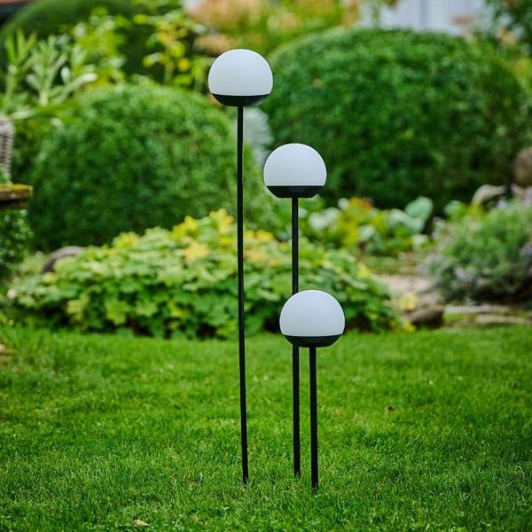 Drei Gartenleuchten mit kugelförmigen Lampenschirmen auf einem Rasen