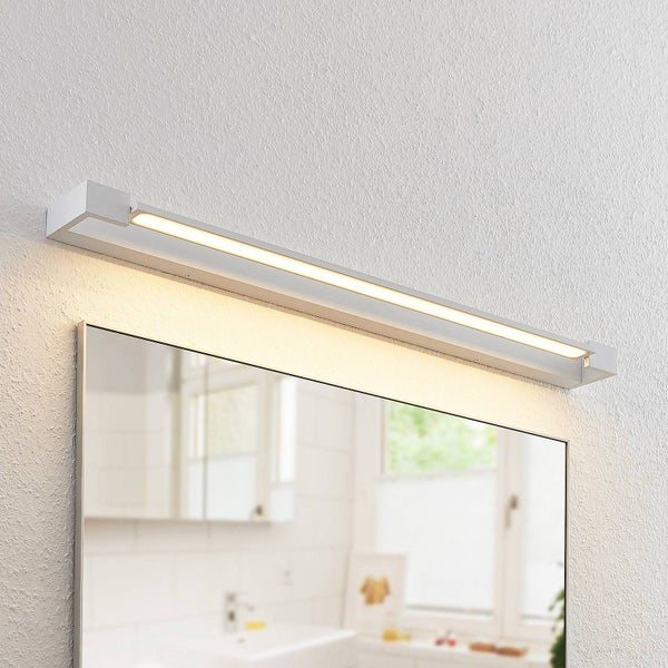 Moderne LED-Spiegelleuchte im Badezimmer, schmales Metallgehäuse, warmweißes Licht, über einem Wandspiegel montiert, helle Atmosphäre.