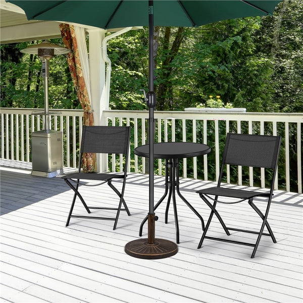 Garten-Bistro-Set auf einer Holzterrasse mit zwei schwarzen Klappstühlen, einem runden Tisch und einem grünen Sonnenschirm mit Ständer.