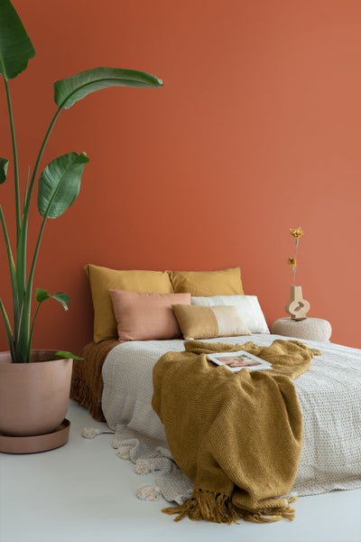 Schlafzimmer mit einer Wand mit vertikalen Streifen in Hellviolett und Terrakotta. Weißes Bett mit Kissen, lila Decke und passendem Nachttisch.