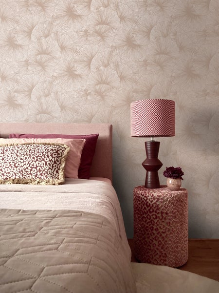 Schlafzimmer mit einer Tapete im Ginkgo-Blatt-Muster, einem Bett mit gemusterten Kissen und einer Tischleuchte auf einem gepolsterten Nachttisch.