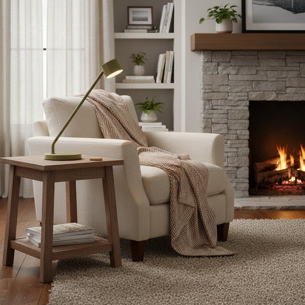 Gemütliche Leseecke mit einem hellen Sessel, einem Holztisch mit Leselampe und einem Kamin im Hintergrund.