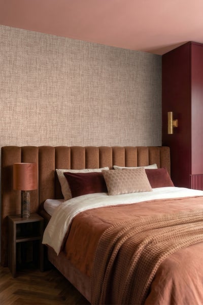 Modernes Schlafzimmer mit strukturierter beiger Tapete, gepolstertem braunem Kopfteil und Bettwäsche in Erdtönen.