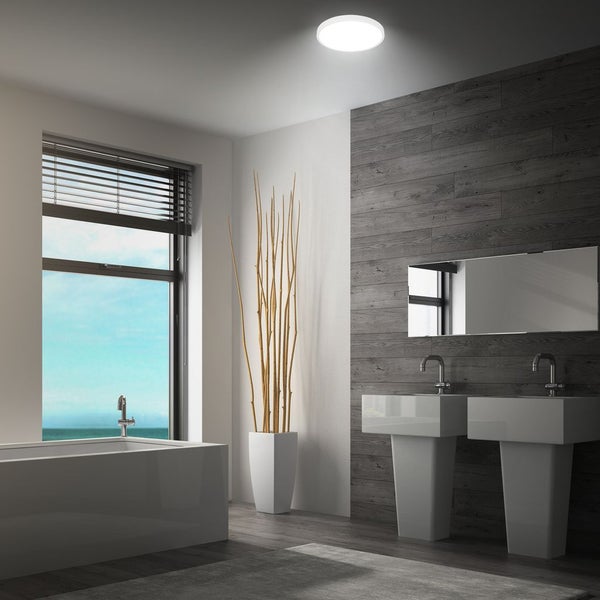 Modernes Badezimmer mit runder Deckenleuchte, zwei Waschbecken, Badewanne, Spiegel und Holzoptik Wandverkleidung.