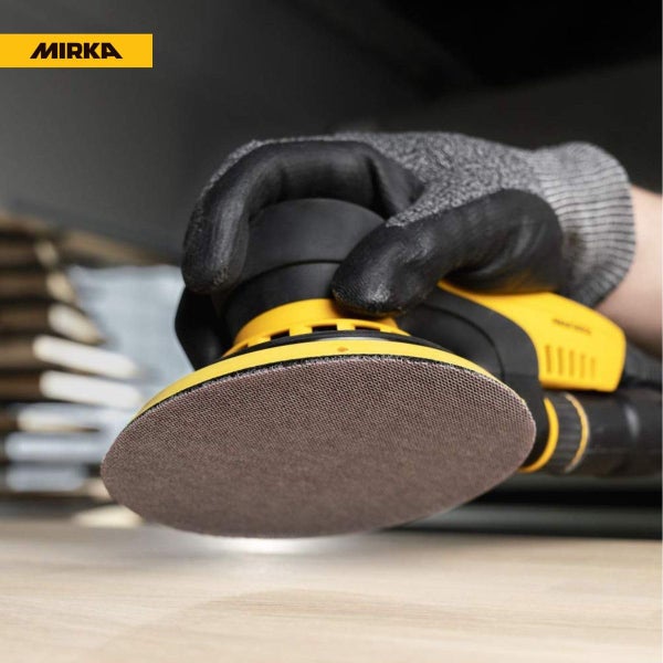 Eine Person mit Schutzhandschuh bedient einen Mirka Exzenterschleifer beim Schleifen einer Holzoberfläche.