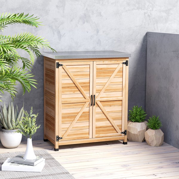Gartenschrank aus Holz mit zwei Türen, X-Design und verzinkter Arbeitsplatte auf einer hellen Terrasse mit Pflanzen arrangiert.