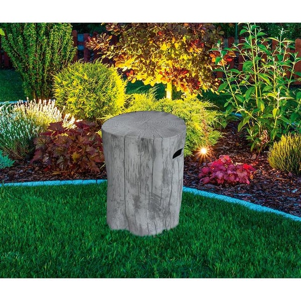 Gartenhocker in Baumstumpf-Optik auf einer Rasenfläche in einem beleuchteten Garten mit verschiedenen Pflanzen und Sträuchern.