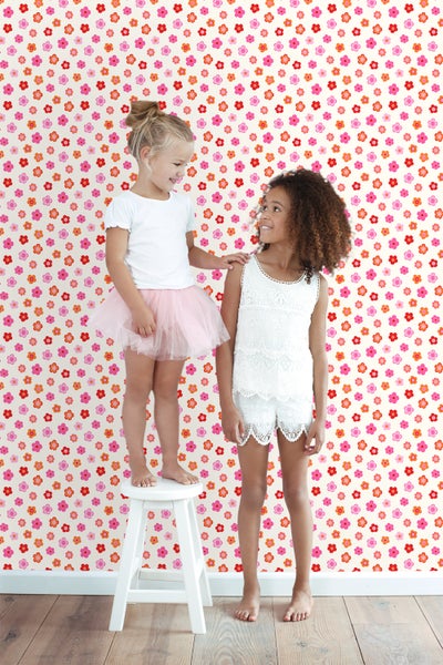 Zwei Mädchen vor einer Wand mit Blumenmuster. Ein Mädchen steht auf einem Hocker.