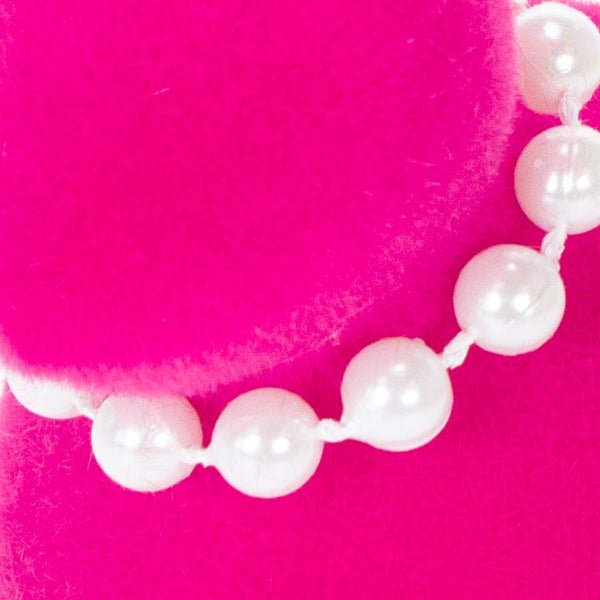 Nahaufnahme einer pinkfarbenen Clutch mit Perlenkette