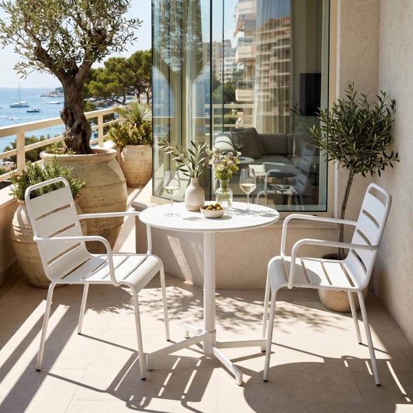 Balkon-Set aus zwei weißen Metallstühlen und einem runden Tisch auf einer hellen Terrasse mit Meerblick und Olivenbäumen.