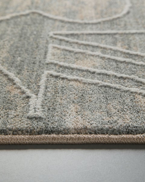 Nahaufnahme eines grau-beigen Teppichs mit Kurzflor, geometrischem Muster aus erhabenen Linien und verstärkter Kante.