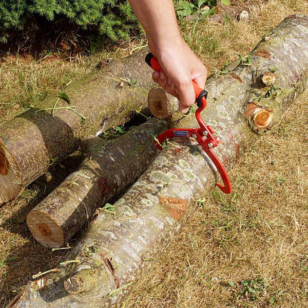 Eine Hand benutzt eine Holzgreifzange, um einen Baumstamm auf einer Wiese zu greifen.