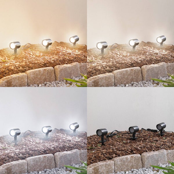 LED-Gartenstrahler in einem Gartenbeet mit Mulch und Steinen, dargestellt mit verschiedenen Lichtfarben von warmweiß bis kaltweiß.