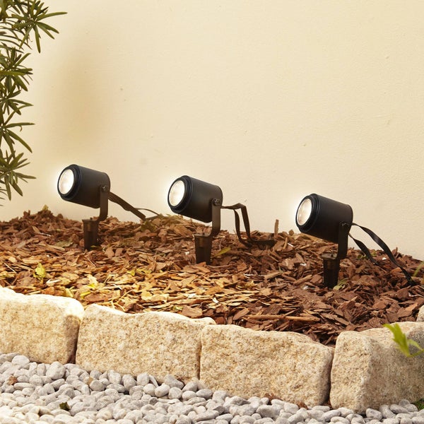 Drei schwarze Gartenstrahler mit Erdspieß in einem Beet mit Rindenmulch und Natursteinbegrenzung.