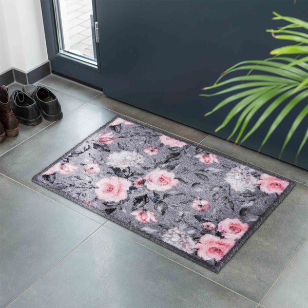 Fußmatte mit Blumenmotiv vor einer Haustür auf Fliesenboden mit Schuhen und Pflanze