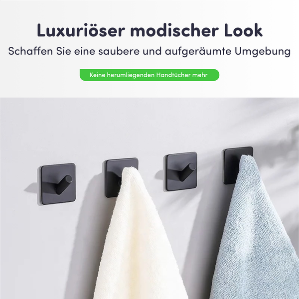 Vier quadratische schwarze Handtuchhaken an einer Wand montiert, zwei davon mit hängenden Handtüchern.