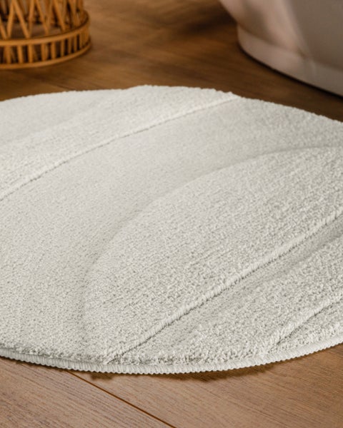 Runder weißer Badeteppich mit strukturiertem Wellenmuster aus weichem Textil.