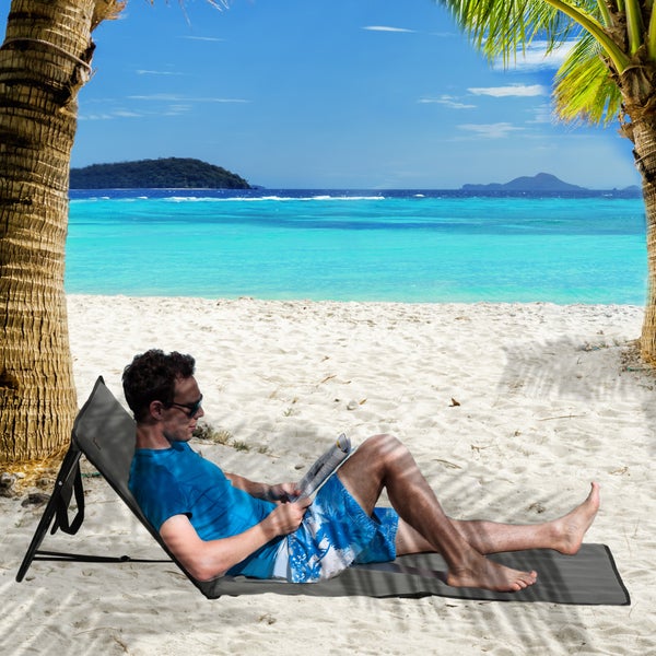 Mann liest Zeitung auf einer Strandliege am Sandstrand mit Blick auf das Meer