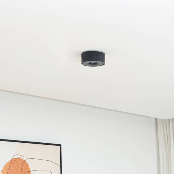 Schwarze, runde Aufputz-Deckenleuchte an einer weißen Decke in einem hellen, modern gestalteten Raum.