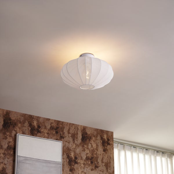 Runde Deckenleuchte mit geripptem Stoffschirm an einer Decke in einem modern eingerichteten, hellen Raum mit strukturierter Wand.