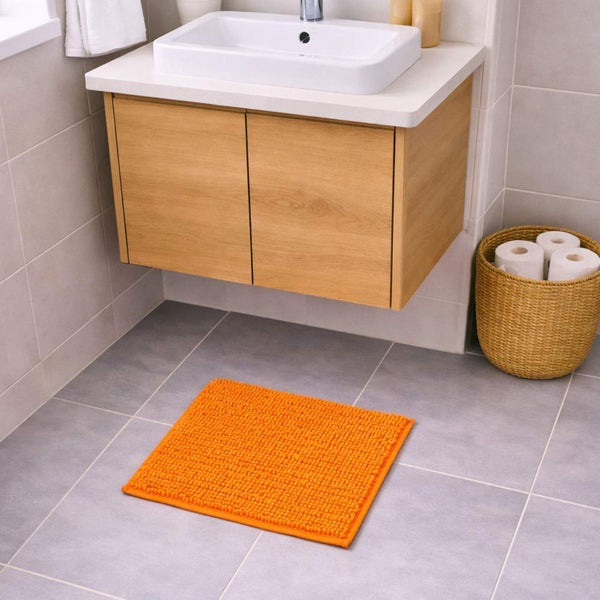 Orangefarbene Badmatte aus Chenille auf grauen Bodenfliesen vor einem Holz-Waschtisch in einem modernen Badezimmer.