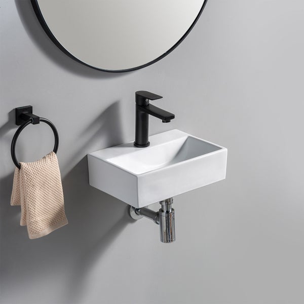 Ein kleines rechteckiges Waschbecken mit einer Wasserarmatur, einem Handtuchring und einem runden Spiegel an einer Wand montiert.