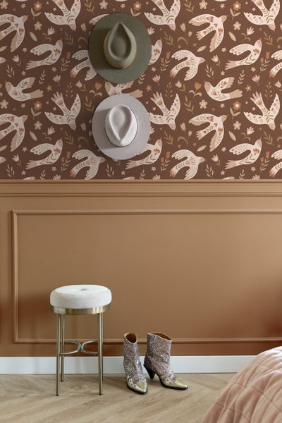 Dekorative Wandgestaltung mit Vogelmuster-Tapete, zwei Hüten und einem Barhocker mit glitzernden Cowboystiefeln