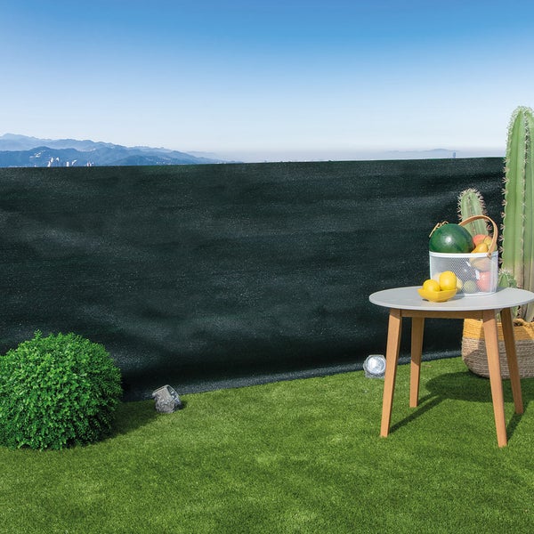 Dunkelgrünes Sichtschutznetz auf einer Terrasse mit Kunstrasen, Beistelltisch, runder Buchsbaumkugel und Ausblick auf Berge.