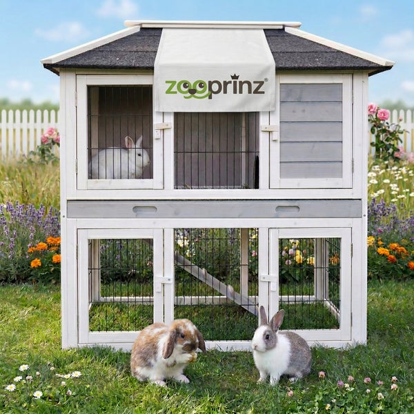 Zweistöckiger Kleintierstall aus weißem und grauem Holz mit Drahtgitter, Rampe und Satteldach im Garten. Zooprinz Logo.