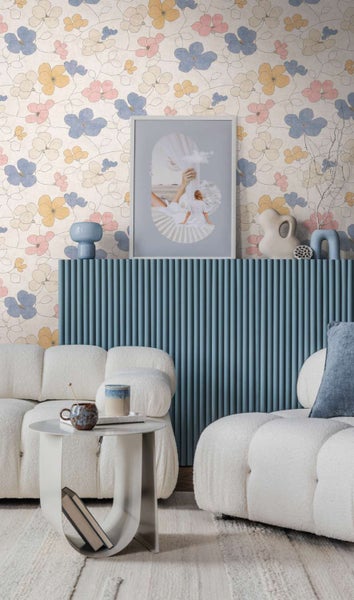 Wohnzimmer mit geblümter Tapete, geripptem Sideboard in Blau und zwei beigefarbenen Boucle Sofas vor einer Wand mit Blumenmuster.