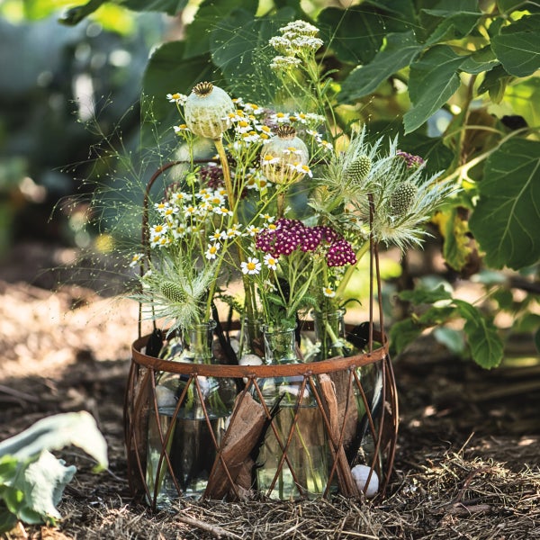Dekorativer Blumenhalter mit Glasflaschen in einem rustikalen Metallgestell, gefüllt mit einer bunten Wiesenblumenmischung im Garten.